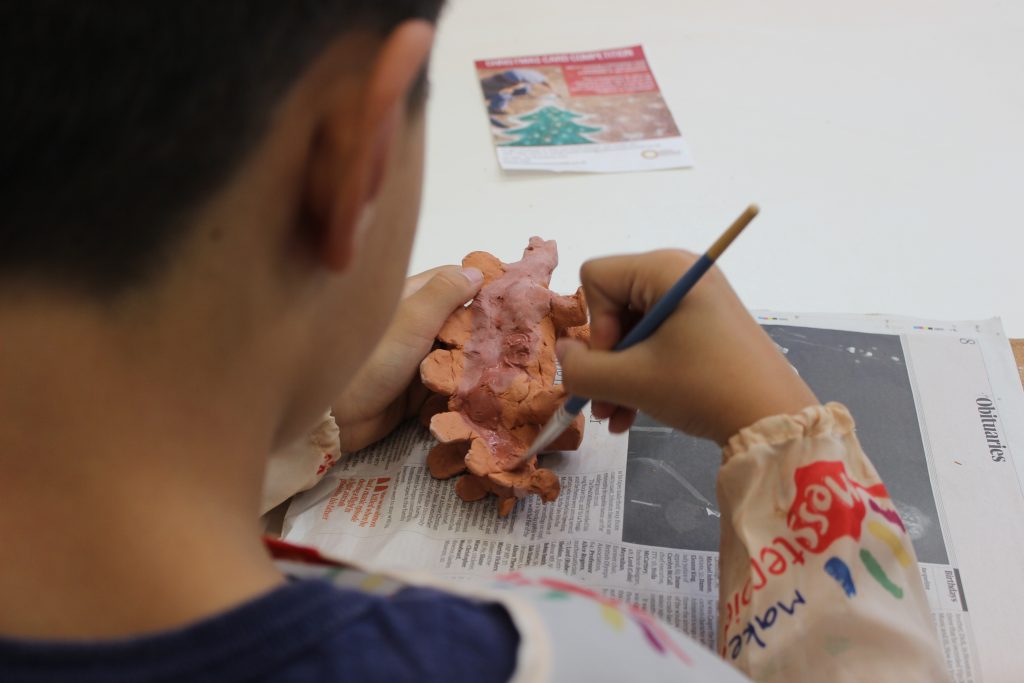 clay, dinosaur, pottery, paint, grey paint, paintbrush, table, newpaper, boy, child